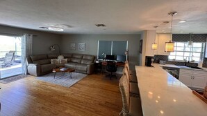 A spacious living area with a large sofa, a coffee table, and a kitchen area with a white countertop and cabinets.