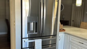A stainless steel refrigerator in a kitchen with white cabinetry and a marble floor.