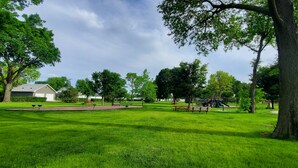 Een park met groen gras, bomen, bankjes en speeltoestellen.