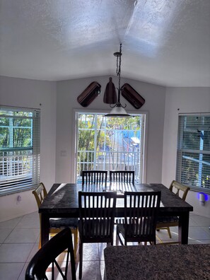 A dining area with a table and chairs, a ceiling fan, and windows with blinds.