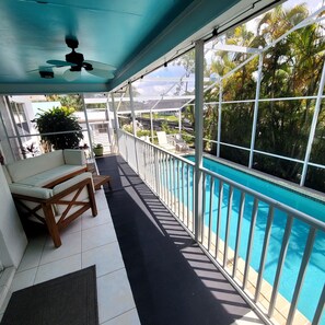 Ein überdachter Balkon mit Pool, weißen Geländern und einem Deckenventilator.