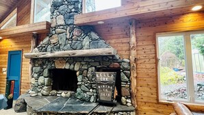 A stone fireplace with a sign reading "Kelly Crk Mining Co. 2010" in a wooden cabin with large windows and a wooden ceiling. - Private Country Paradise with Beautiful Indoor Pool and Spa. PET FRIENDLY (Cave Junction)