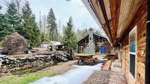 A wooden cabin with a stone chimney, a wooden deck, and a stone bridge over a stream. - Private Country Paradise with Beautiful Indoor Pool and Spa. PET FRIENDLY (Cave Junction)
