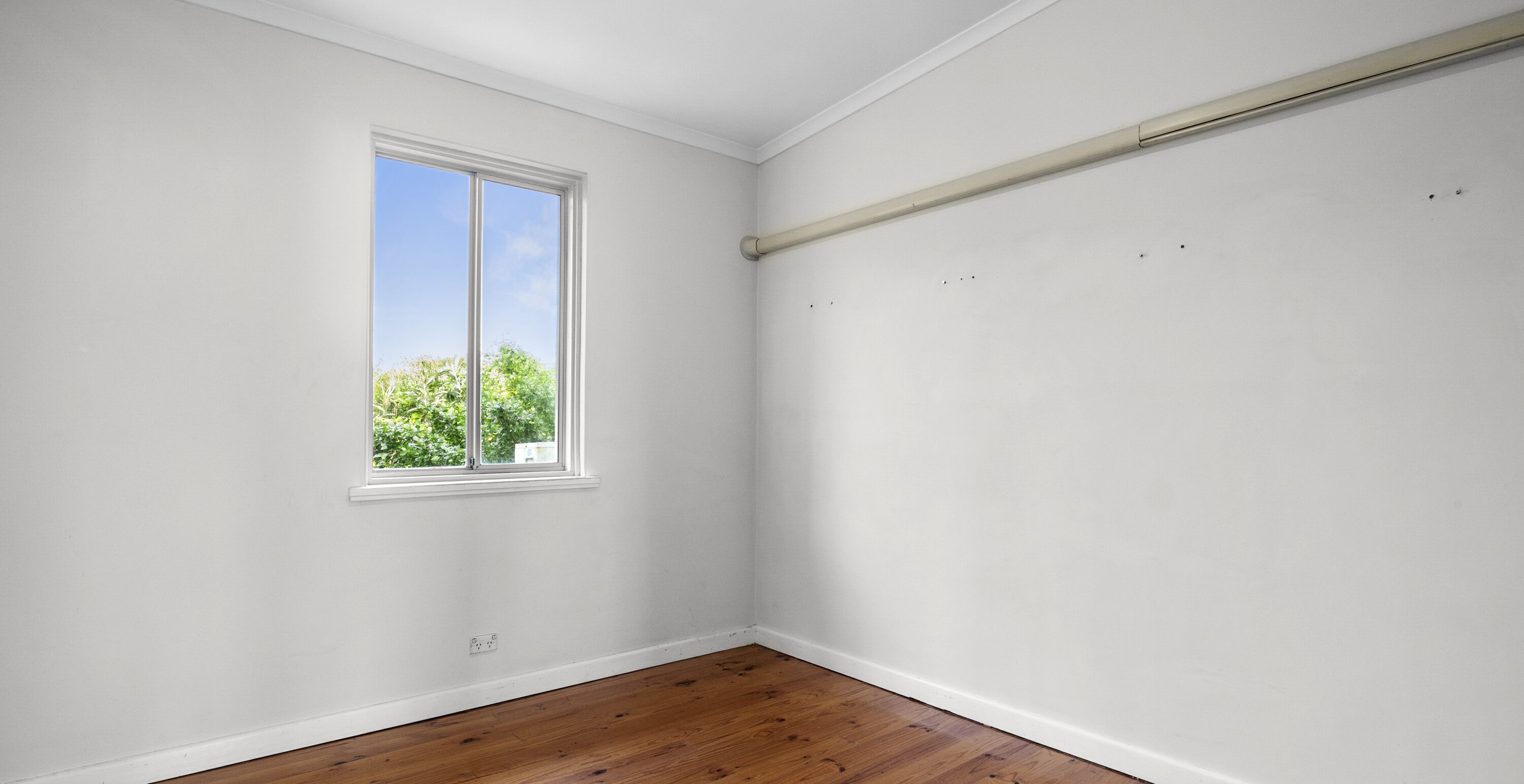 Une pièce aux murs blancs, avec un plancher en bois, une grande fenêtre donnant sur les arbres et un plafond où l’on peut voir les conduits.