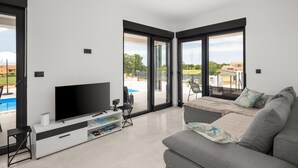 A modern living room with a flat-screen TV, a sofa, and a dining area.