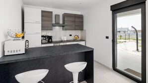 A modern kitchen with a dark countertop, white bar stools, and a view of the outside through a glass door.