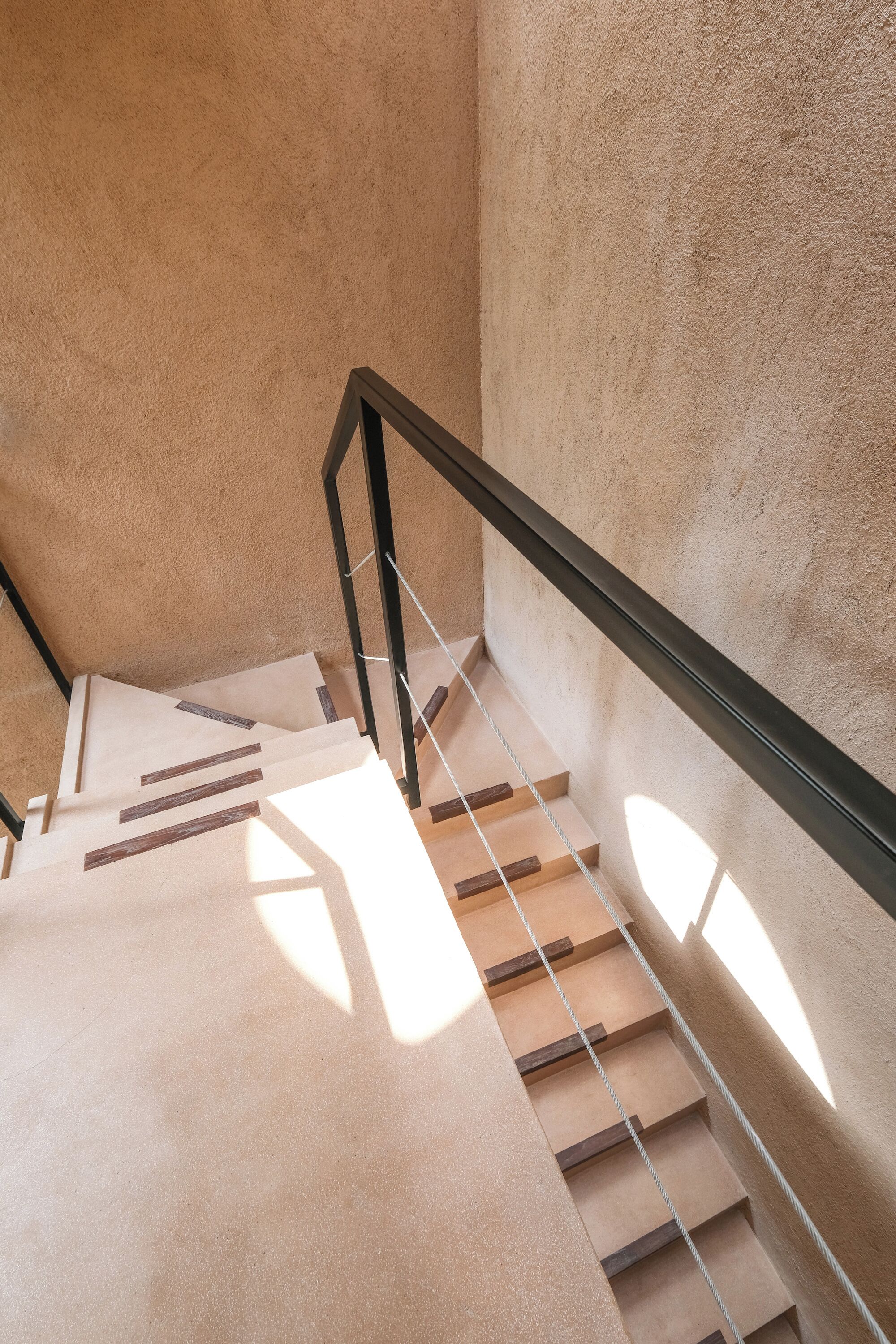 A staircase with wooden steps and a black handrail, leading to a higher floor.