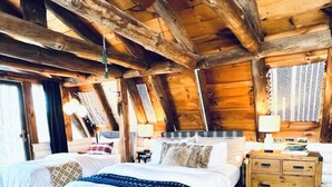 Un dormitorio de cabaña de troncos con una cama grande, dos camas más pequeñas, un aparador de madera y una alfombra de cuero de vaca.