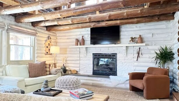 Amplia sala de estar con chimenea de piedra, vigas de madera, televisor y asientos cómodos.