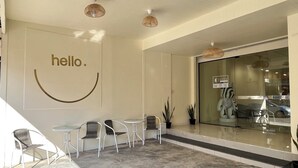 Zona de recepción con un letrero que dice 'hello', asientos y una puerta de vidrio que da a un estacionamiento.