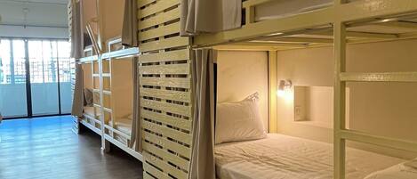 Un dormitorio con literas, suelo de madera y ventana con cortinas.