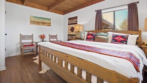 A wooden bed with a colorful blanket, a chair with a red cushion, and a window with curtains.