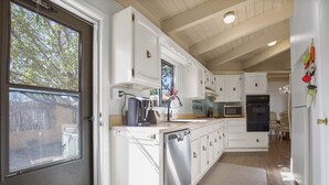A kitchen with white cabinets, a dishwasher, a sink, and a window overlooking a backyard.