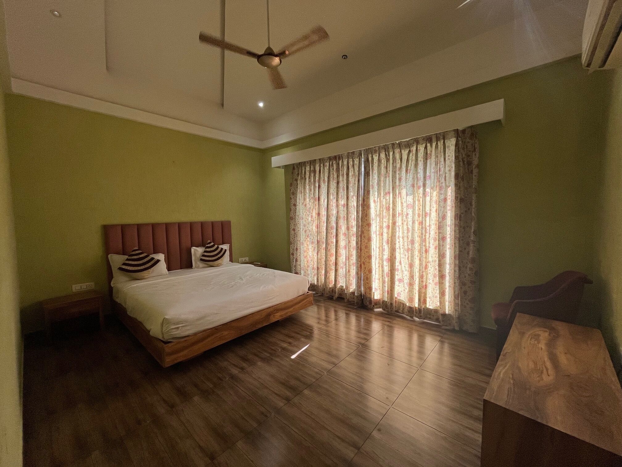 A bedroom with a wooden bed, green walls, a ceiling fan, and a large window with curtains.