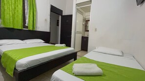 Een hotelkamer met twee bedden, elk met een groene plaid en witte kussens. Er is een deur naar een badkamer en een kitchenette.
