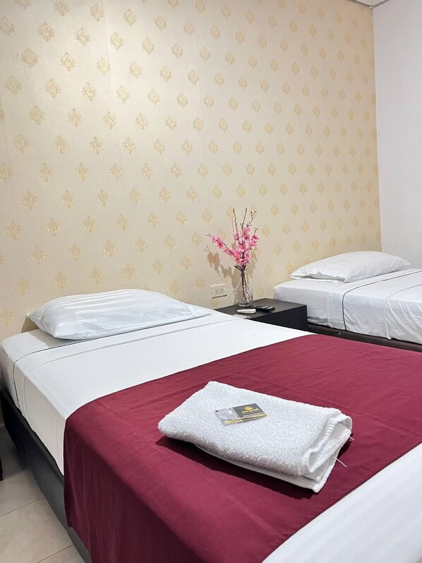 A hotel room with two beds, a red bedspread, a white towel, and a vase with pink flowers on a nightstand. - Casa Dorada Hotel Boutique (Neiva)
