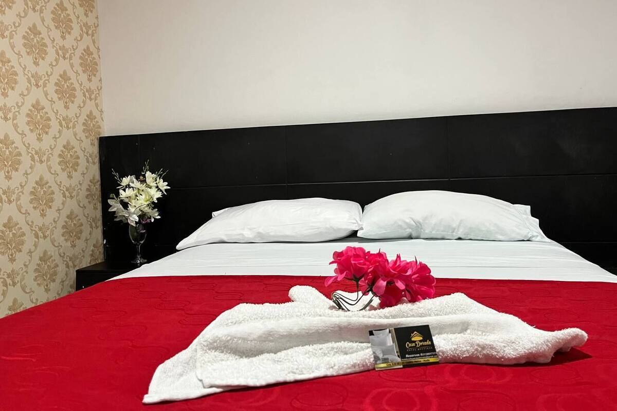 Une chambre d’hôtel avec un lit bien fait, une couvre-lit rouge, des oreillers blancs et un petit vase avec des fleurs.