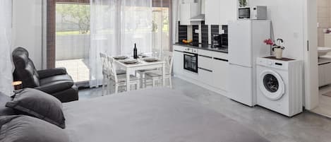 A modern bedroom with a large bed, a dining area with a table and chairs, a kitchen with appliances, and a laundry area.