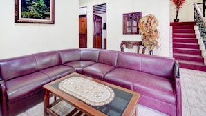 Ein Wohnzimmer mit einem violetten Ledersofa, einem Couchtisch mit Glasplatte, einem gerahmten Bild an der Wand, einer Treppe und einem Topf mit Pflanze.