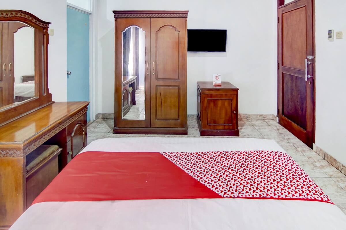 Een slaapkamer met een bed, een houten garderobe, een spiegel, een televisie en een klein kastje.