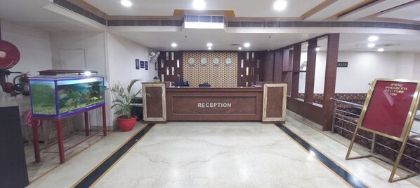 Welcome to Grand Sandareya, where guests are greeted by a beautifully designed reception area featuring a central desk, a fish tank, and a potted plant.
