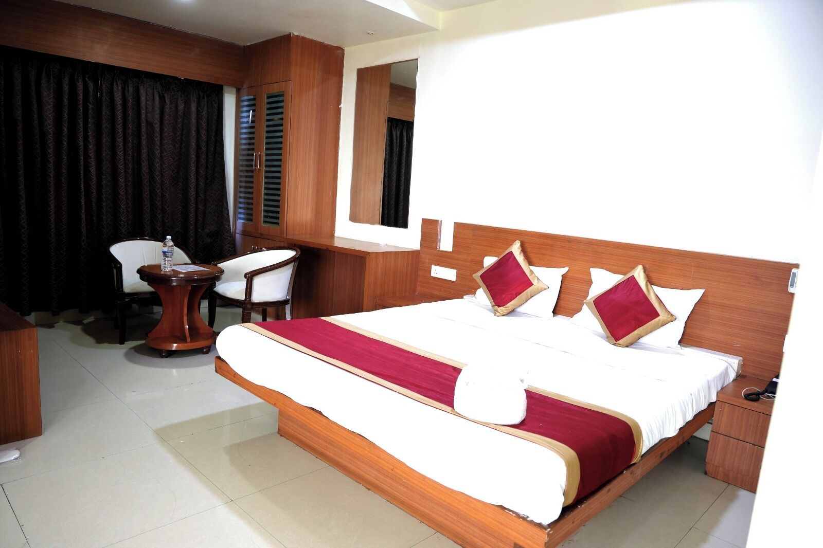 A hotel room with a large bed, a desk, a chair, and a mirror.