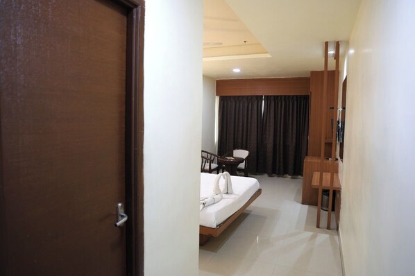 Une chambre d’hôtel avec un lit, un bureau et une chaise. Une porte donne accès à une autre pièce.