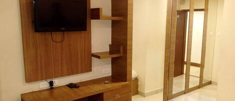A modern room with a wooden TV stand, a flat-screen TV, a wooden desk, and a sliding glass door leading to a bathroom.