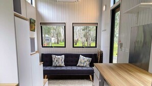 A compact kitchen with a built-in seating area, wooden flooring, and large windows offering views of the outdoors. - Tiny Away Escape at Grampians Edge (Dadswells Bridge)