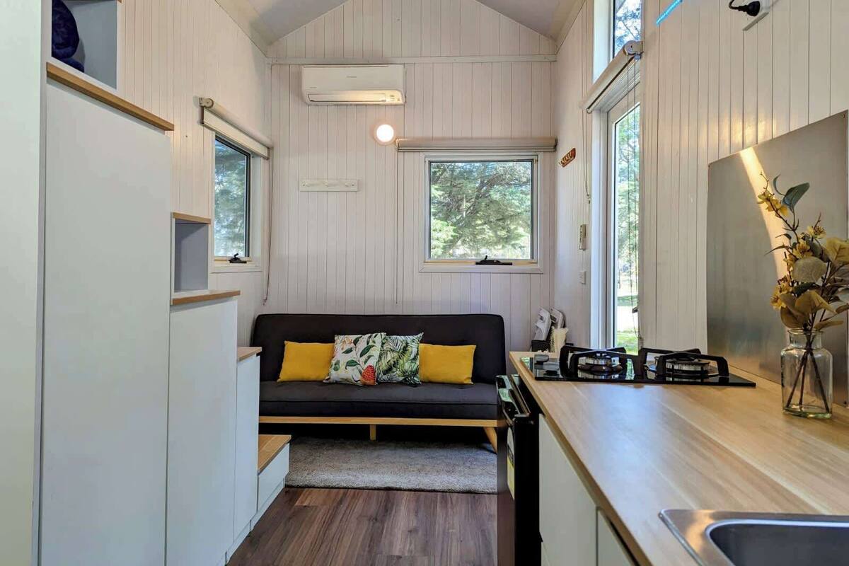 Un espacio habitable compacto con sofá, kitchenette y ventana que proporciona luz natural.