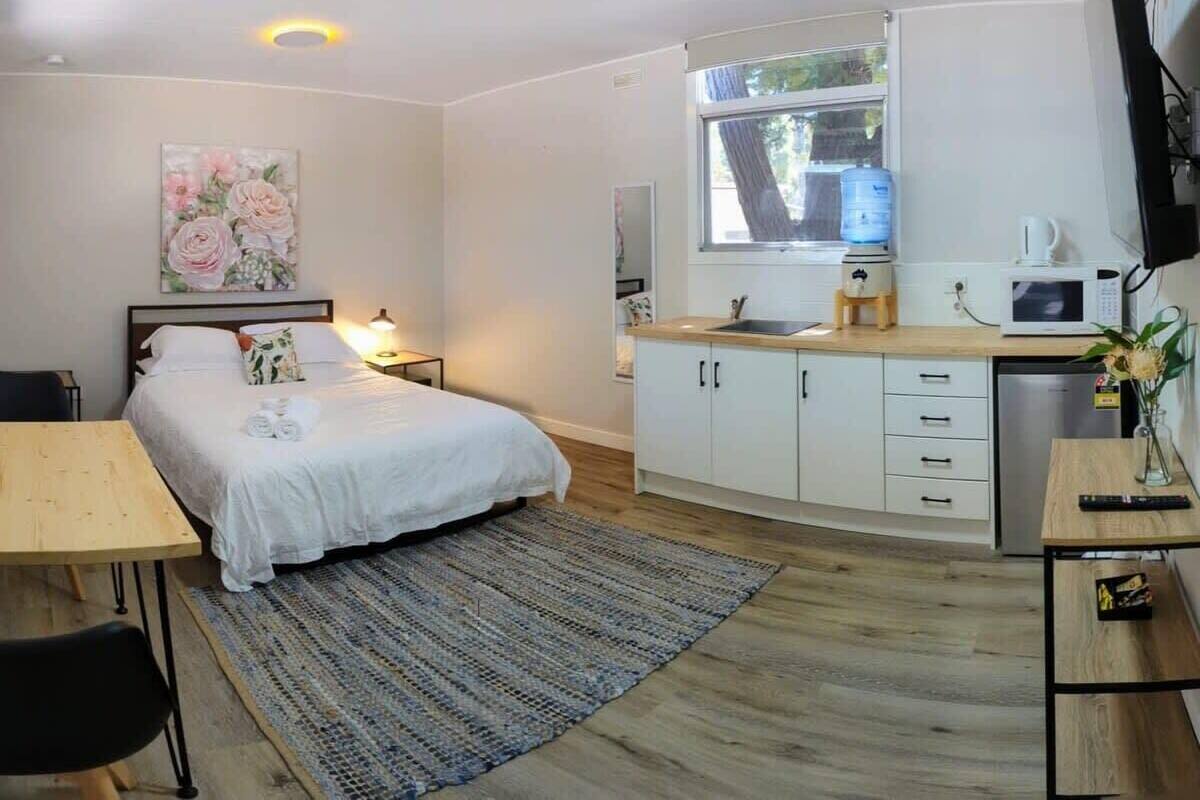 Una habitación de hotel pequeña con cama, mesita de noche y una kitchenette.