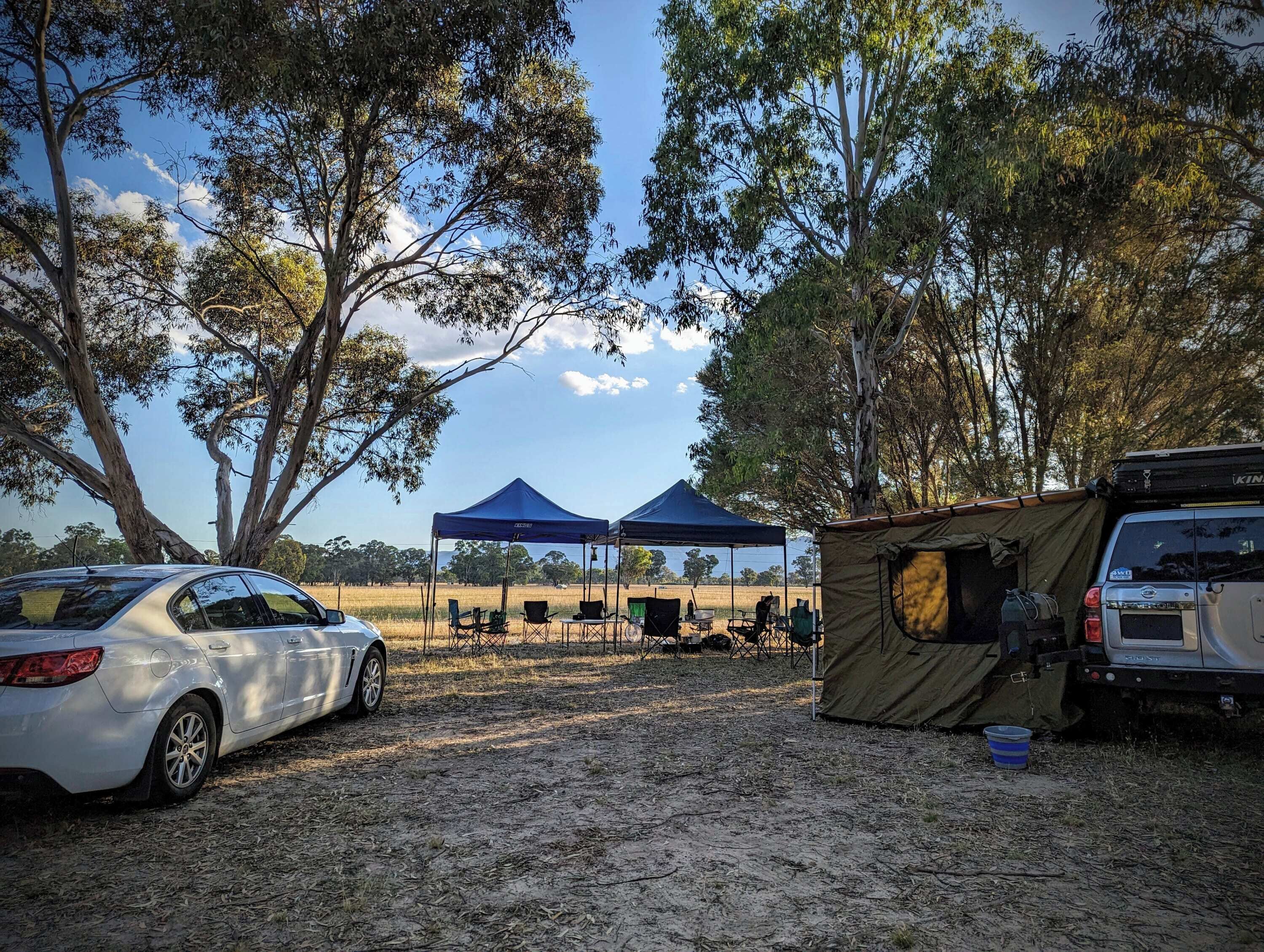 Un terrain de camping avec des tentes, une voiture et une table sous un auvent bleu.