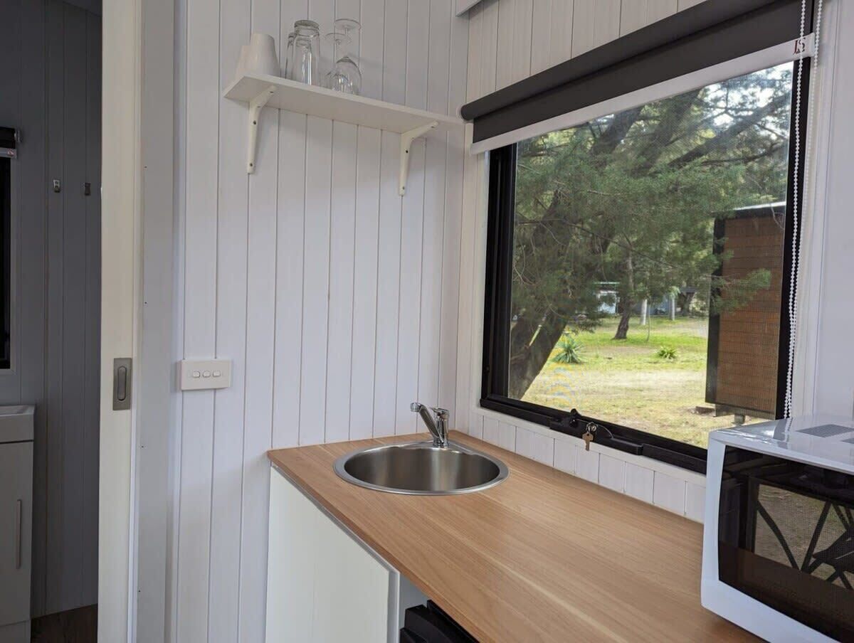 A compact kitchen with a stainless steel sink, wooden countertop, and a window overlooking a garden.