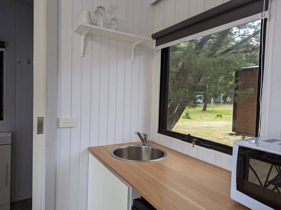 A compact kitchen with a stainless steel sink, wooden countertop, and a window overlooking a garden.