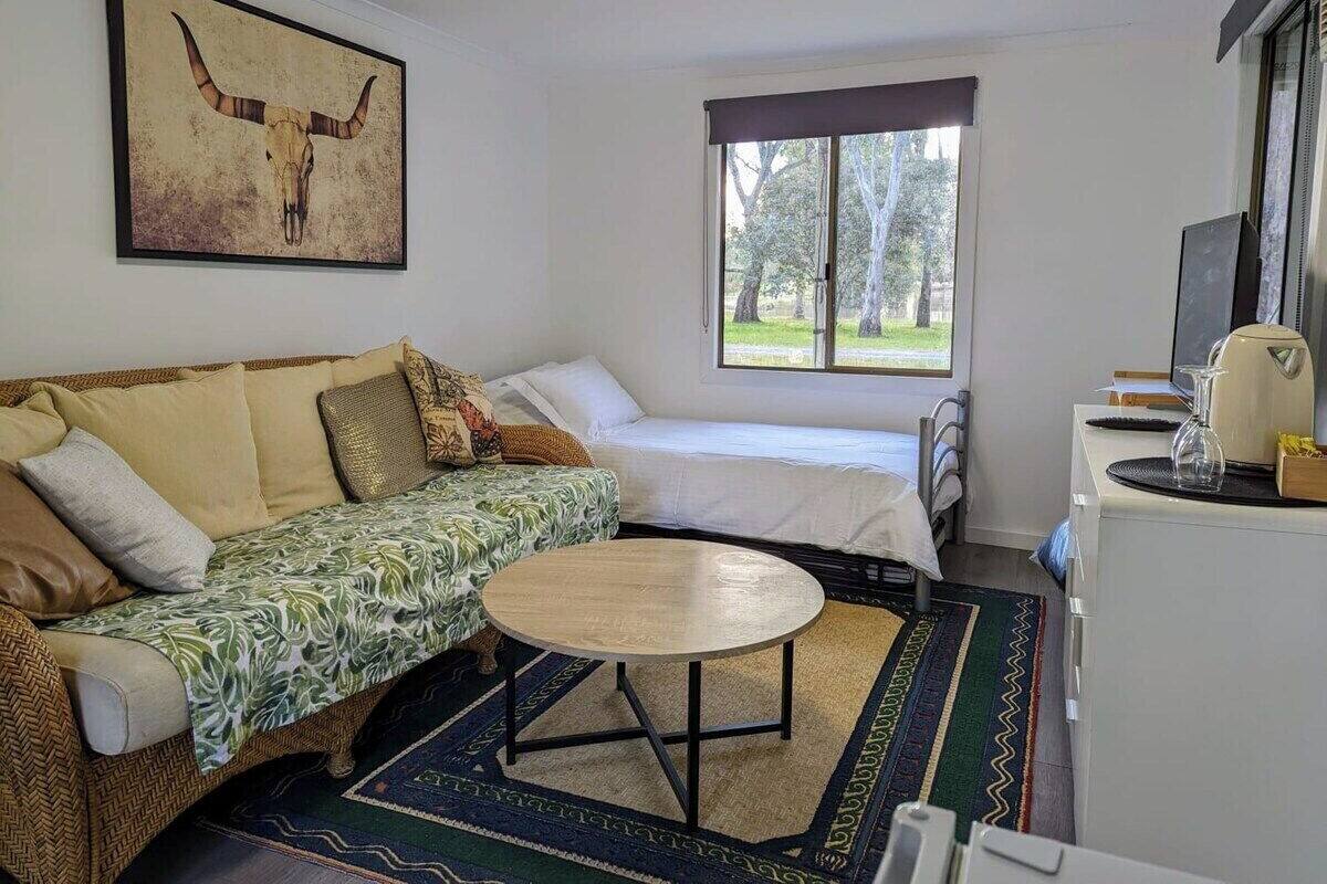 Habitación acogedora con sofá, cama, una mesita y ventana con vista a árboles.
