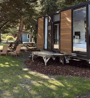 A modern, compact cabin with a wooden exterior and large windows, featuring a small porch and outdoor seating area. - Tiny Away Escape at Grampians Edge (Dadswells Bridge)