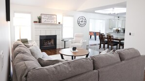 Un salon moderne avec une cheminée, un coin repas et une cuisine en arrière-plan.