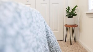 Une chambre à coucher avec un lit, une porte blanche, une petite table avec une plante et une fenêtre.