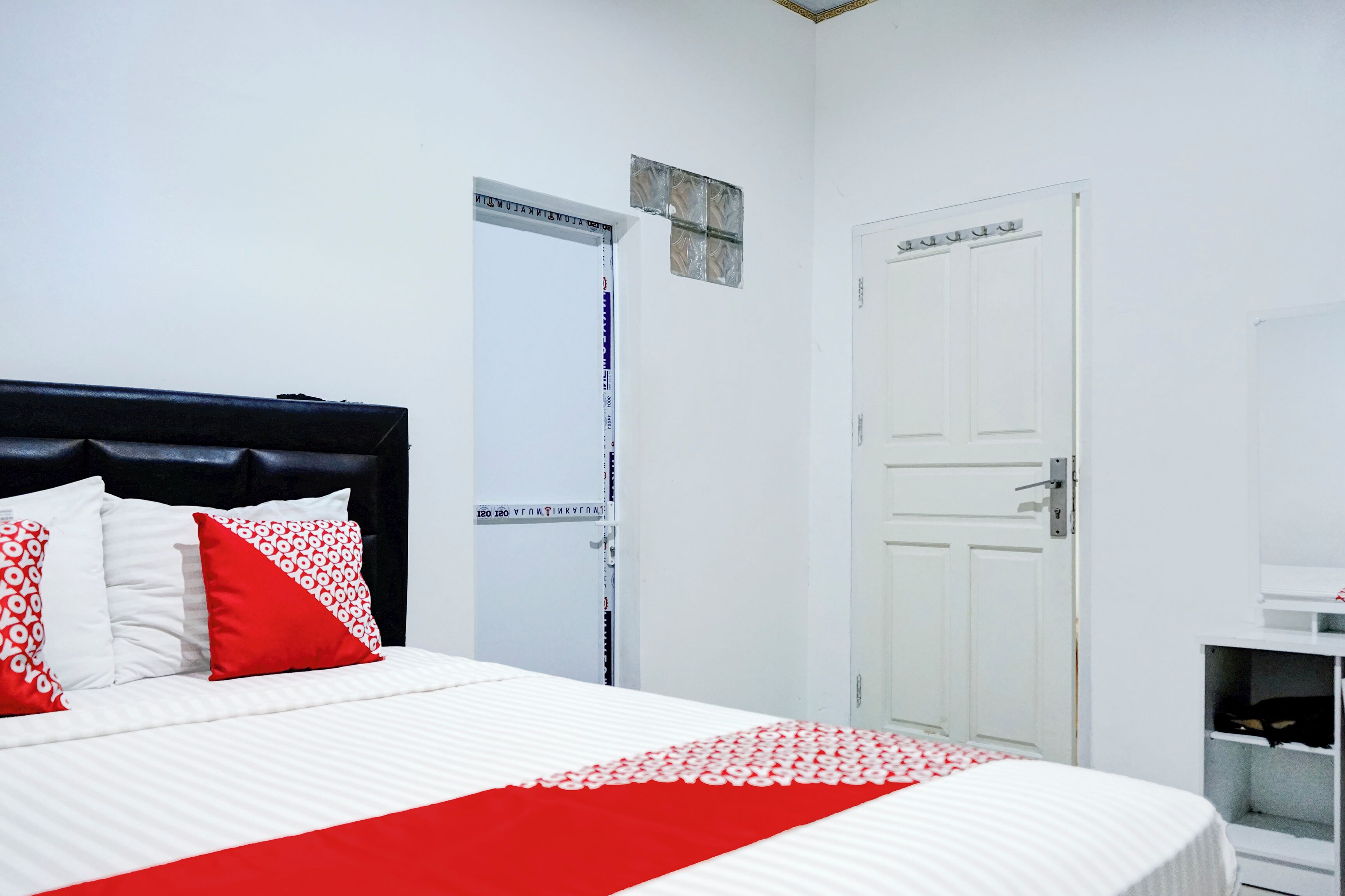 A hotel room with a bed, white walls, a black headboard, and a white door.