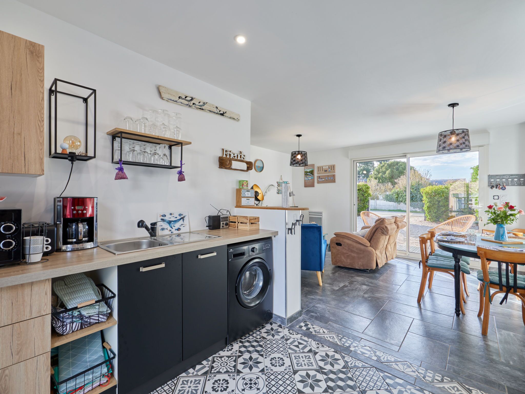 A modern kitchen with a washing machine, a coffee machine, and a dining area with a table and chairs.
