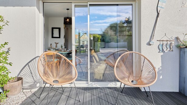 A patio with two wicker chairs, a table, and a glass door leading to an outdoor area.