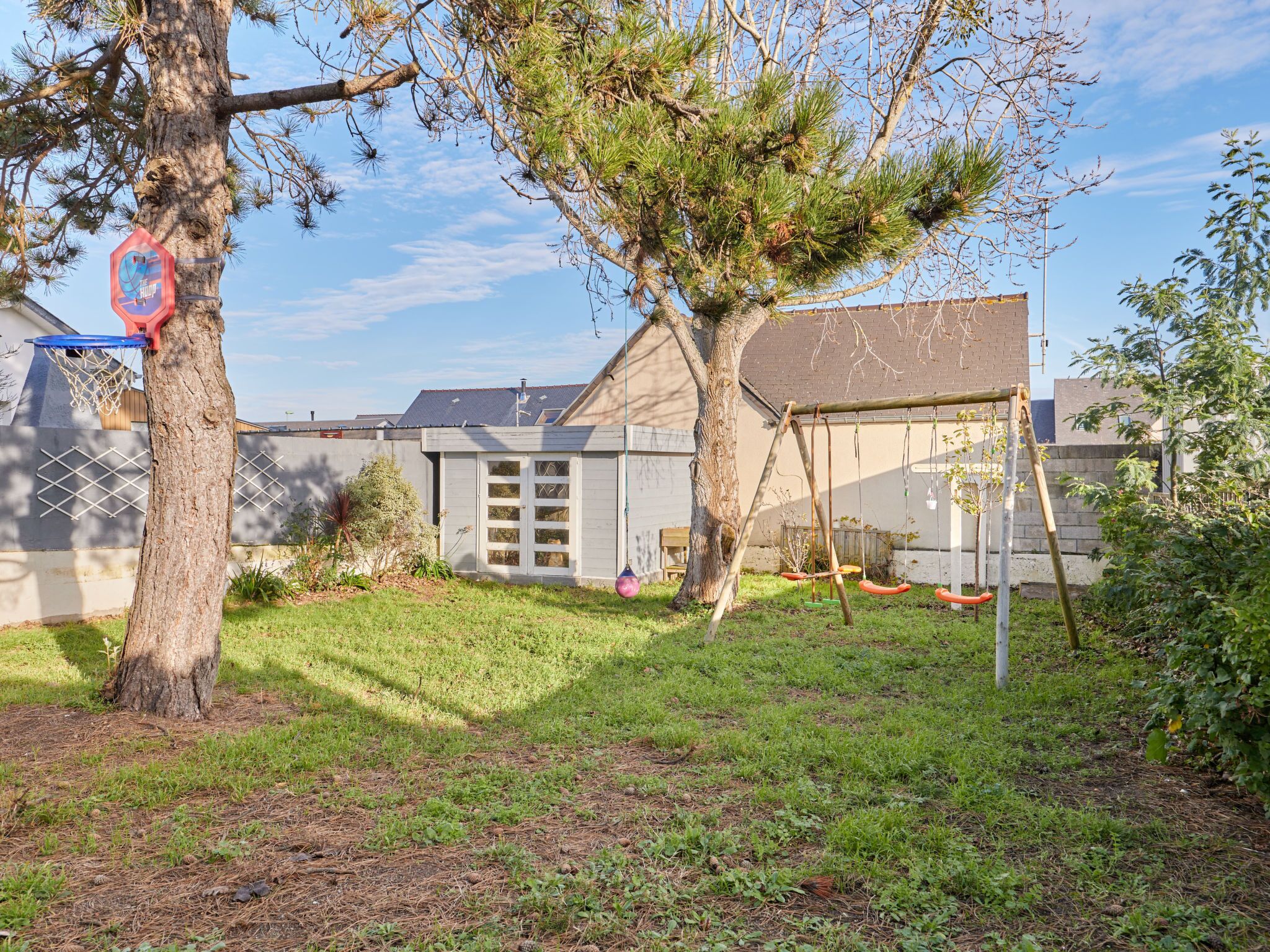 A residential backyard with a basketball hoop, a swing set, and a small garden area.