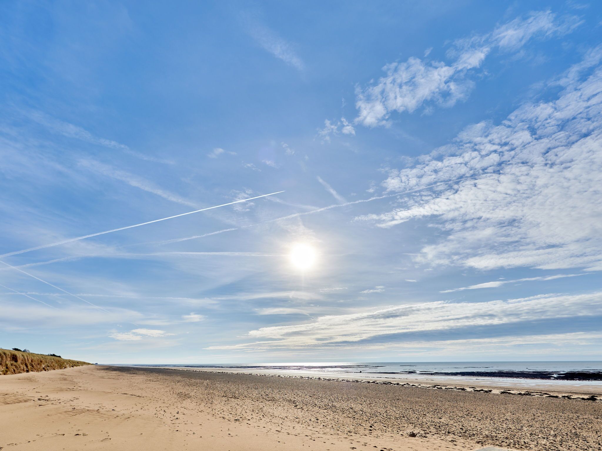 Una playa con cielo despejado, estelas visibles y una costa distante.