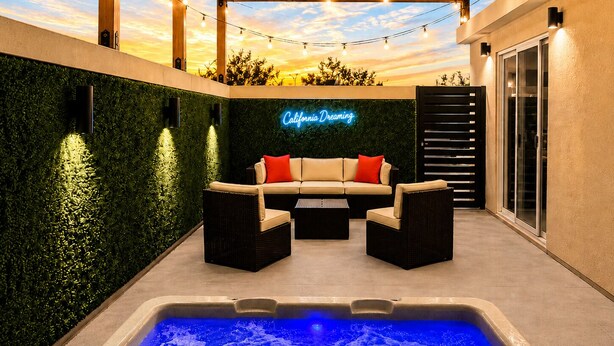 Eine Terrasse mit Pool, einer Neonreklame, Gartenmöbeln und einer Pergola.