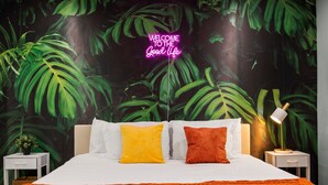 Ein Schlafzimmer mit einem Bett, zwei Kissen, einem Nachttisch, einer Lampe und einem Wandgemälde.