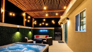 Eine Dachterrasse mit Whirlpool, Sitzgelegenheiten im Freien, Lichterketten und einem Neonzeichen.