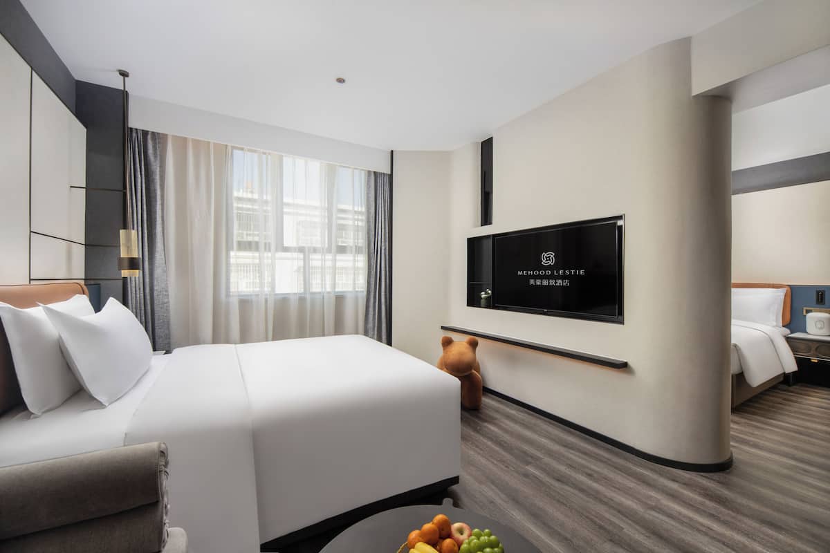 Una habitación de hotel moderna con una cama grande, un televisor de pantalla plana montado en la pared, una mesita de noche y una ventana con cortinas.