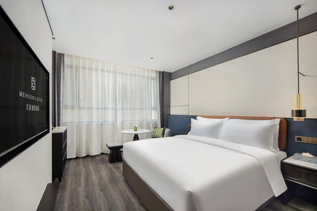 Habitación de hotel moderna con una cama grande, un escritorio y una pantalla de televisión mostrando la marca del hotel.