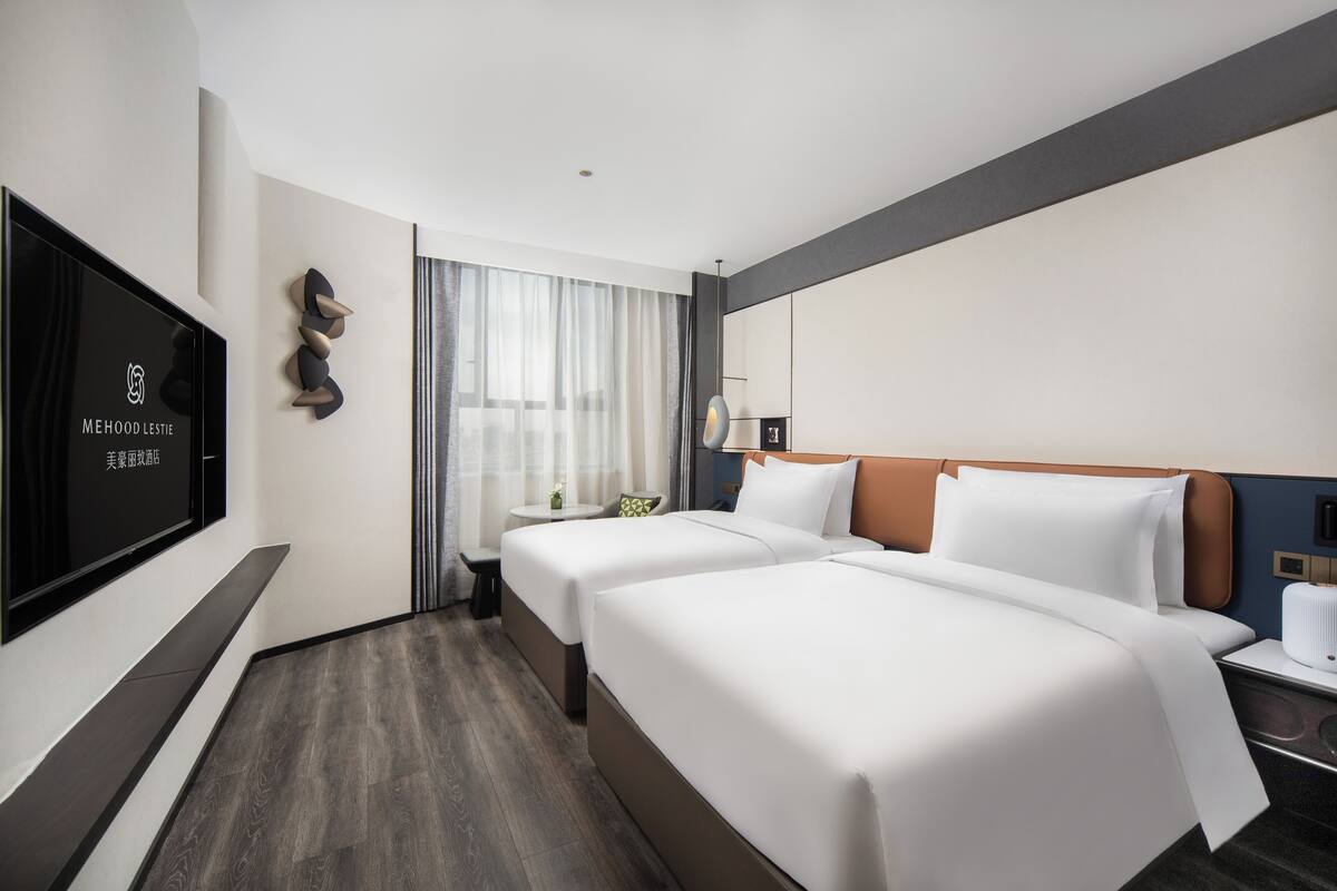Habitación de hotel con dos camas, televisión, escritorio y ventana con cortinas.