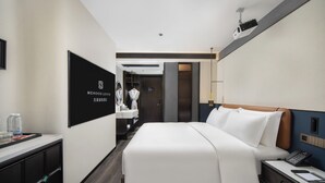 Ein Hotelzimmer mit einem großen Bett, einem Schreibtisch mit Telefon und einem an der Wand befestigten Fernseher.